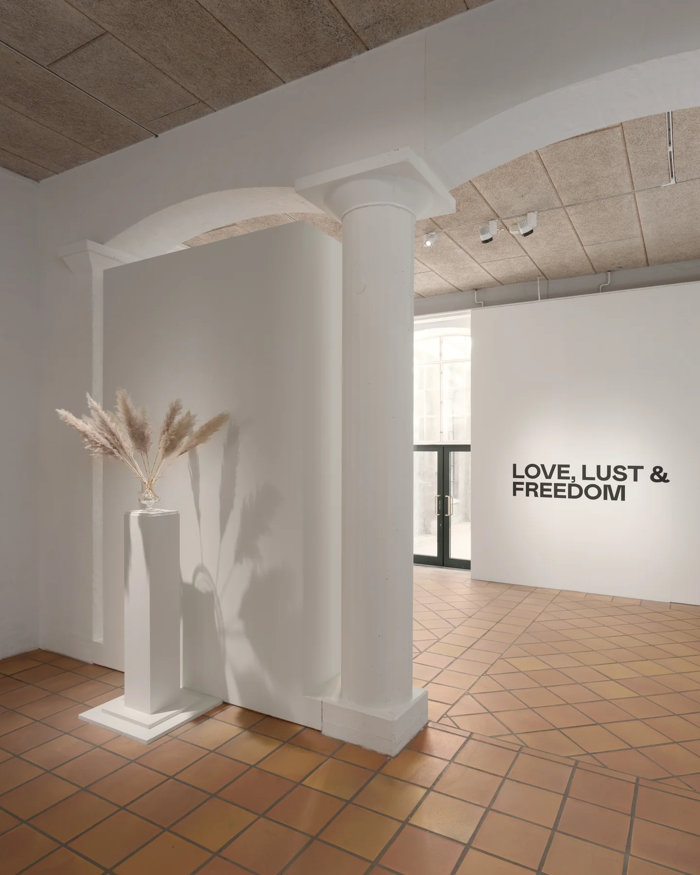 Installation view: the entrance to Love, Lust and Freedom, the exhibition title painted on the wall beyond an archway.