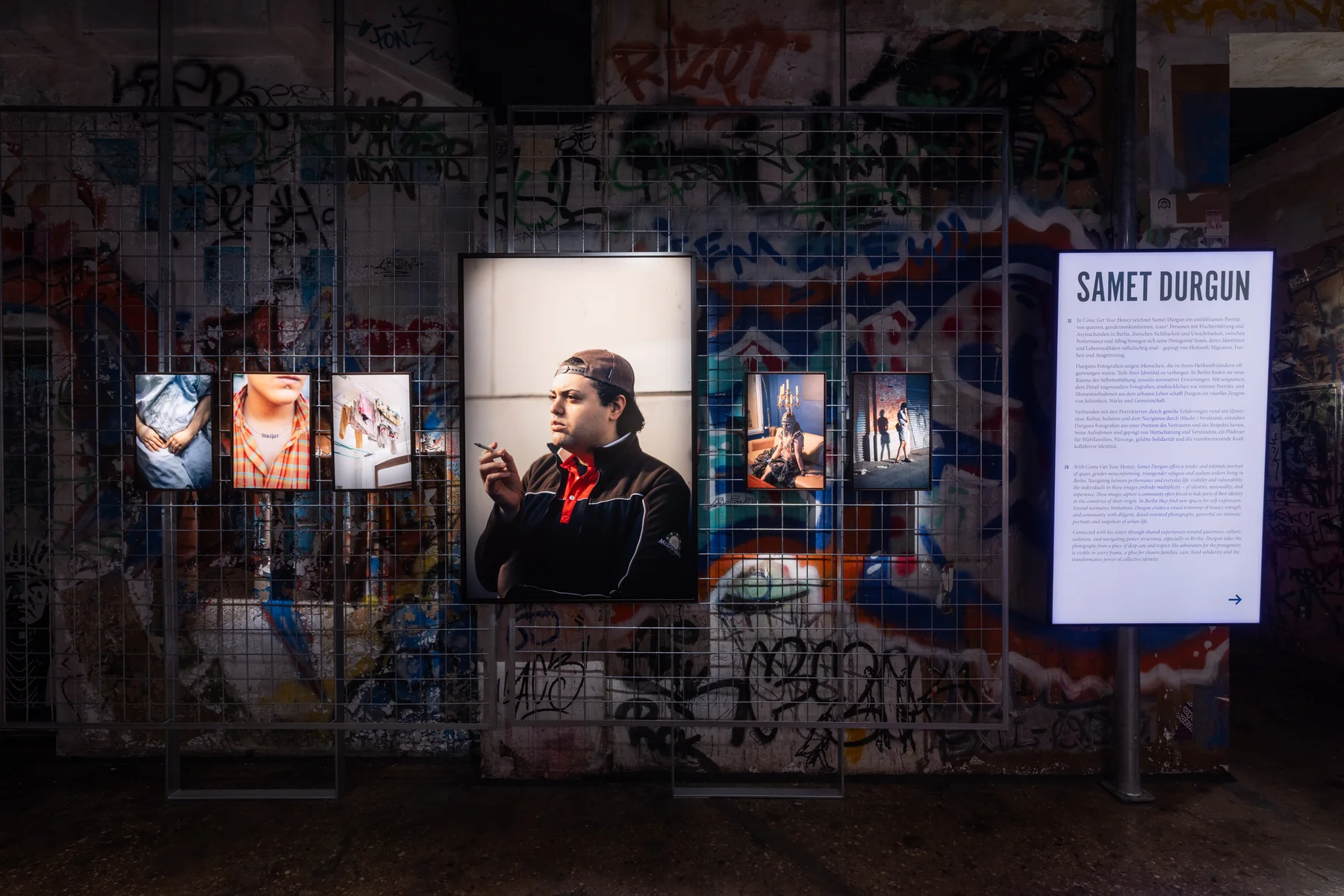 Installation view: prints from Come Get Your Honey mounted on a graffiti-covered wall, beside a wall panel reading Samet Durgun.