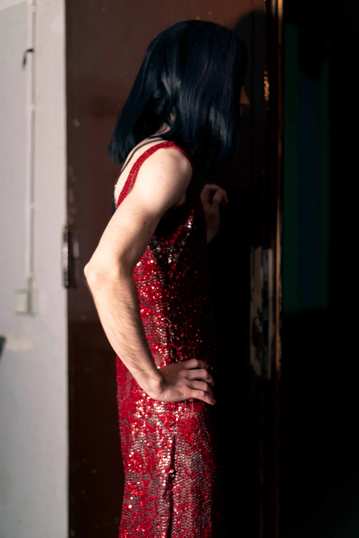 A person in a red sequinned dress stands in a doorway, seen from behind.