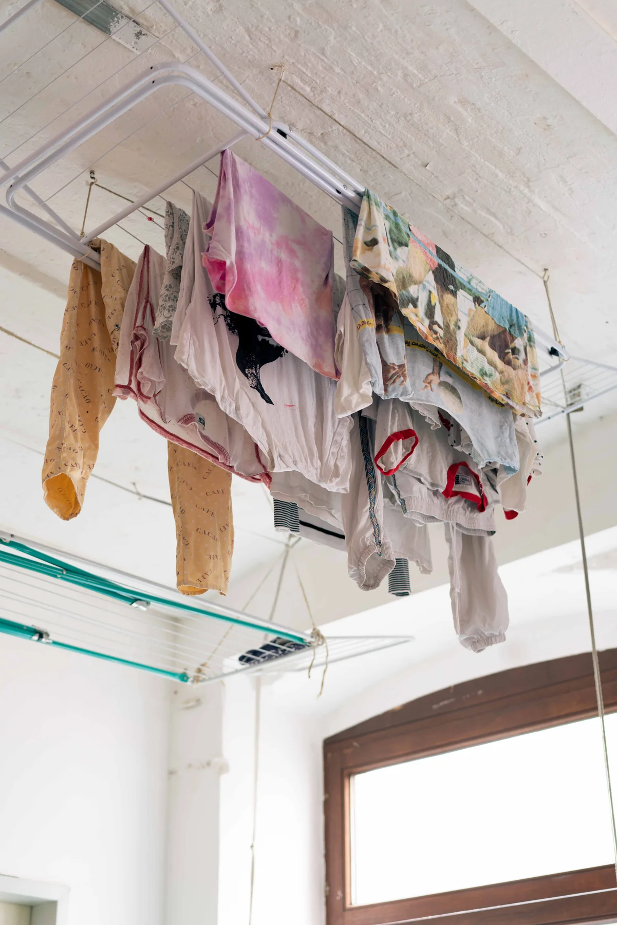 Laundry hangs on lines strung across a bright room with white brick walls.