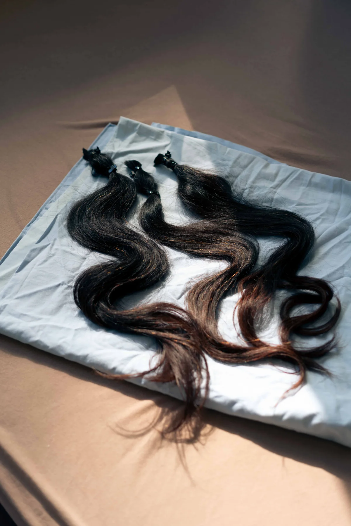 Long dark hair extensions laid out on a white sheet.
