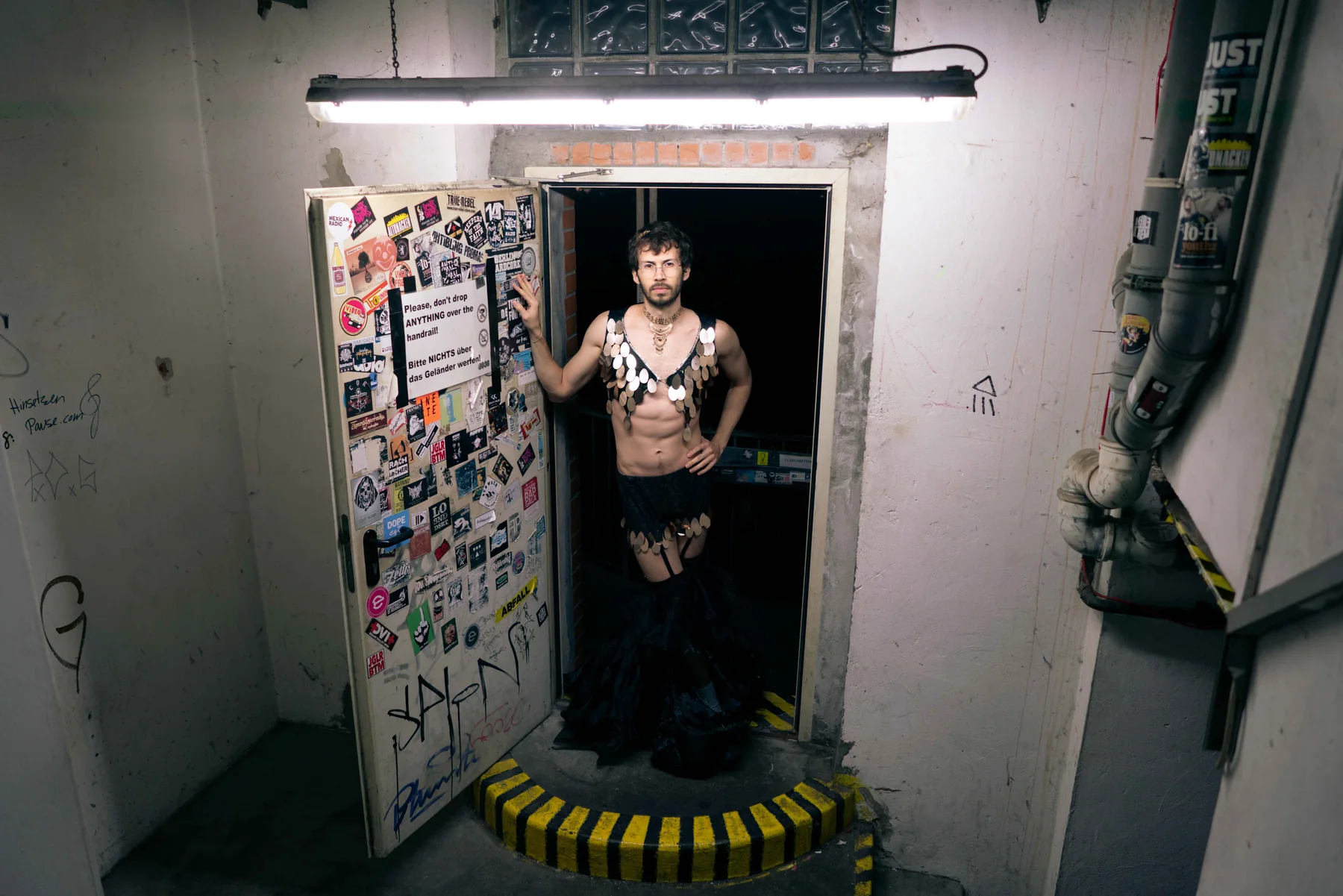 A person stands in a lit basement doorway covered in stickers.