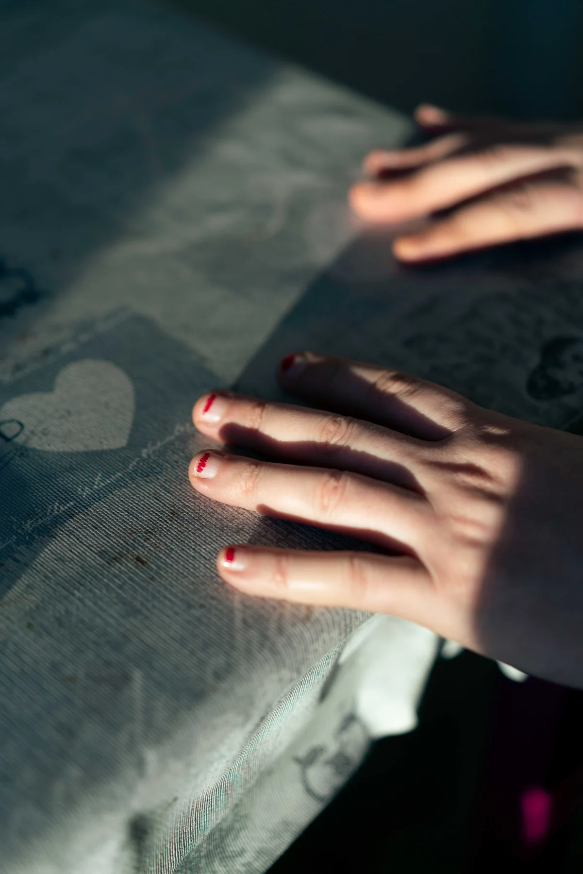 Two hands rest together on a bed in low afternoon light.