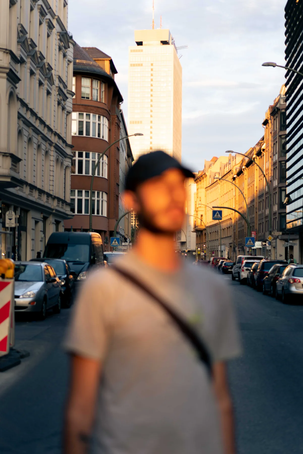A figure stands out of focus in a Berlin street, low sun catching the buildings behind.