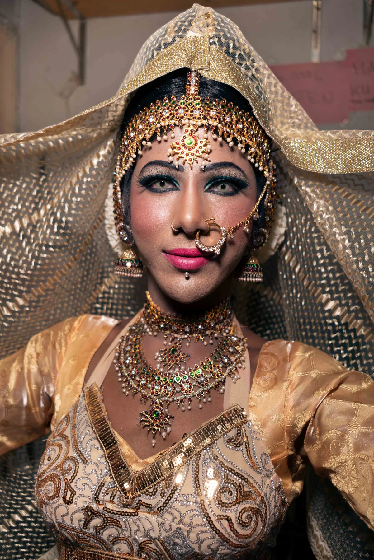 A portrait in a gold bridal headdress and layered jewellery, eyes meeting the camera.