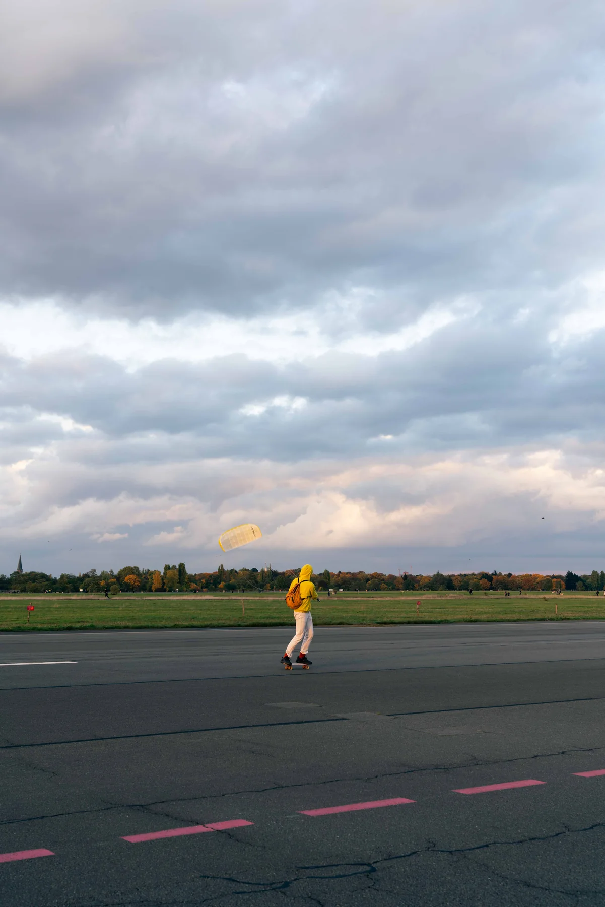 A skater crosses Tempelhof field in a yellow jacket under heavy clouds.